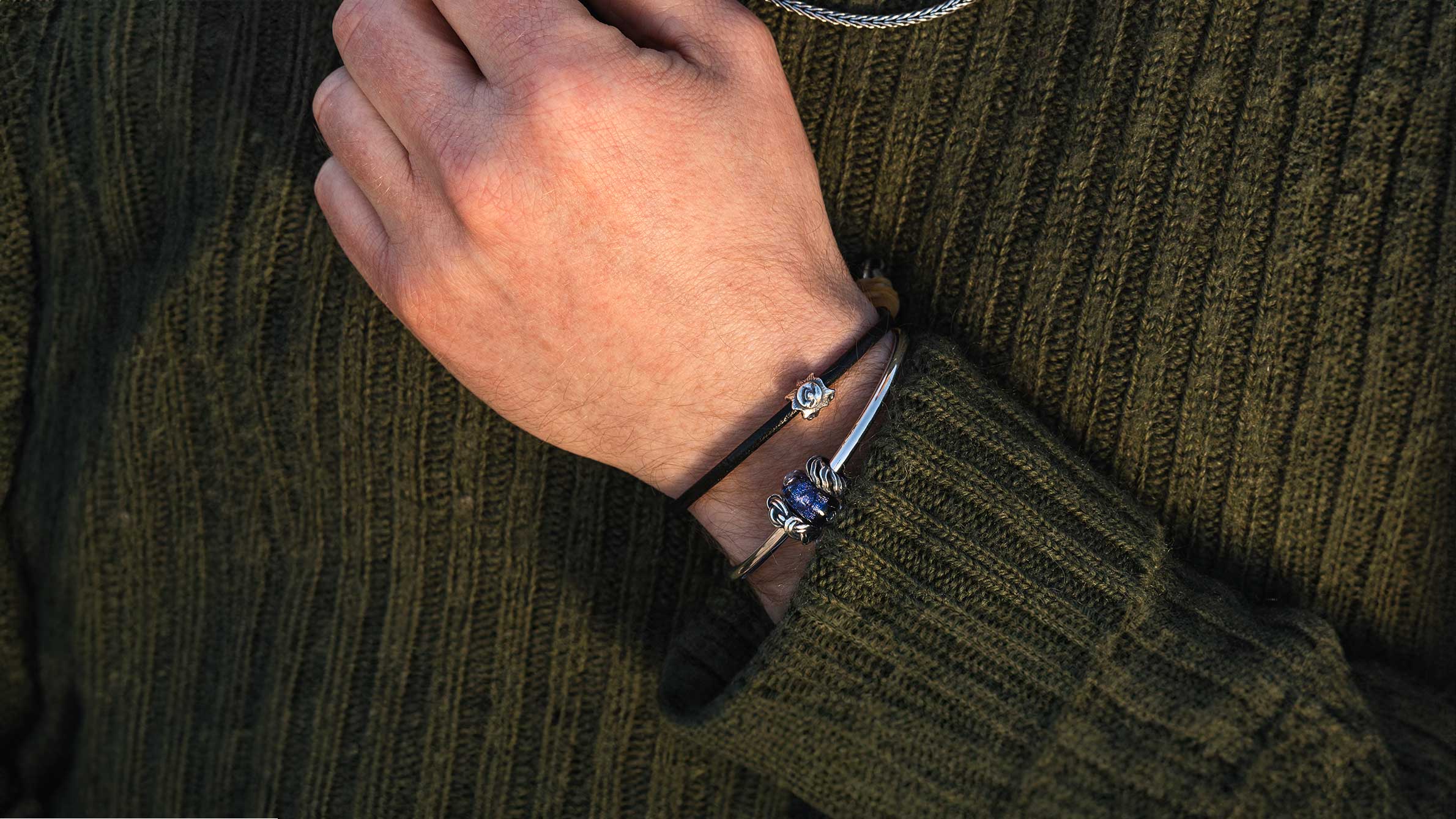 Trollbeads Sunshine silver bead on a leather bracelet complemented by a silver bangle with a blue glass bead and two silver spacers on a male model wearing a green knit sweater